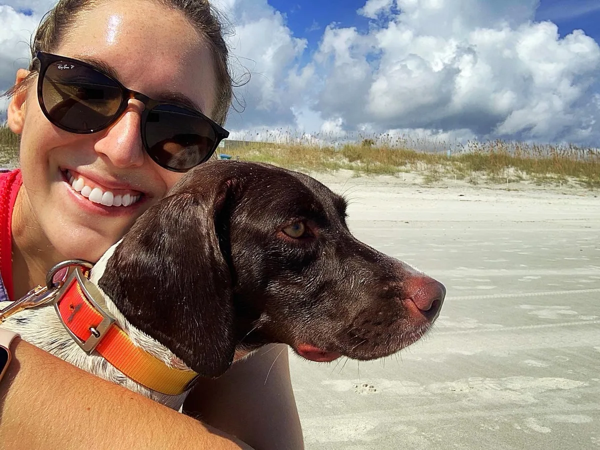 Dolly, a German shorthaired pointer, resting her head against her owner&rsquo;s shoulder on the beach.
